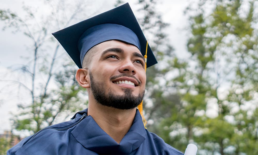 Hombre con birrete y toga azul sosteniendo un diploma en la graduación